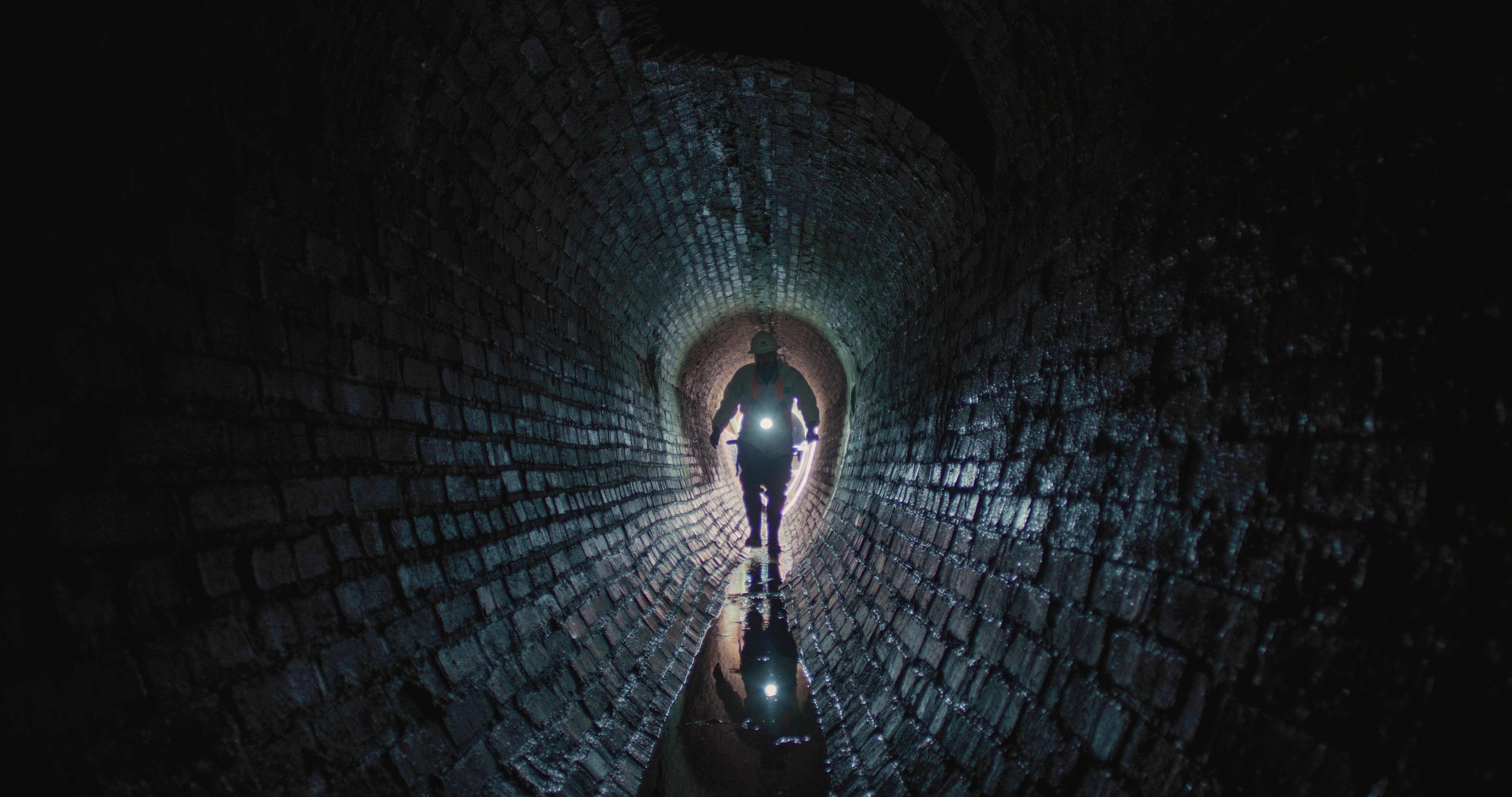 man walking through an old wastewater sewer
